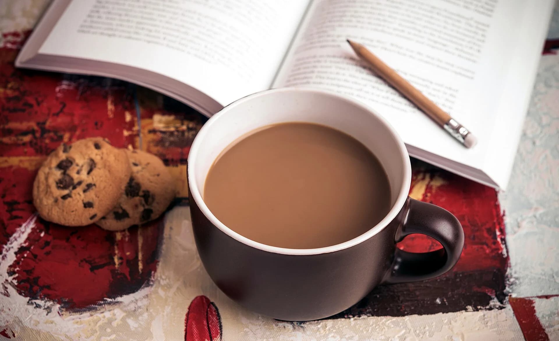 An open book and pencil beside coffee and cookies
