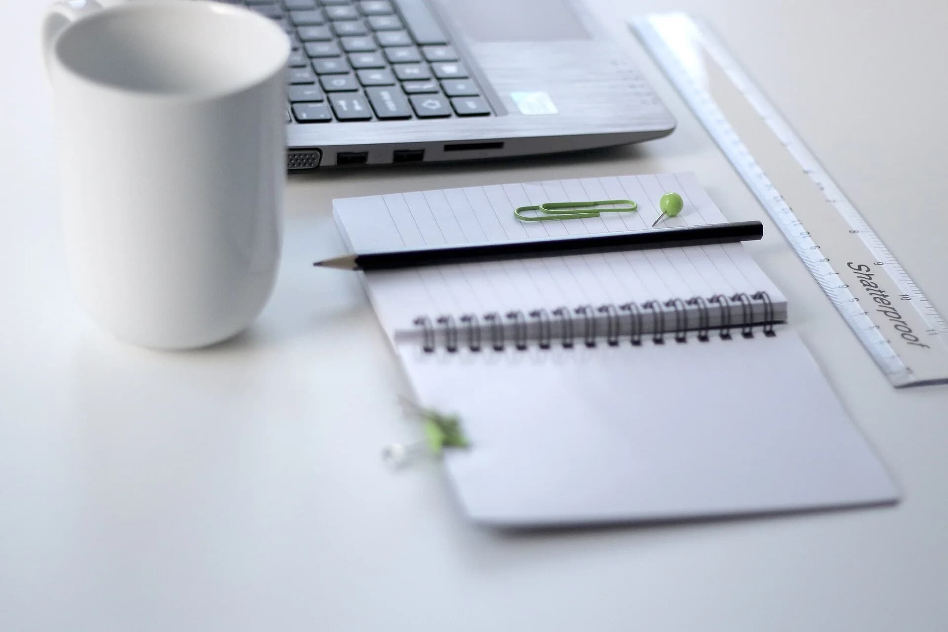 A notebook, pen and ruler beside a laptop and mug