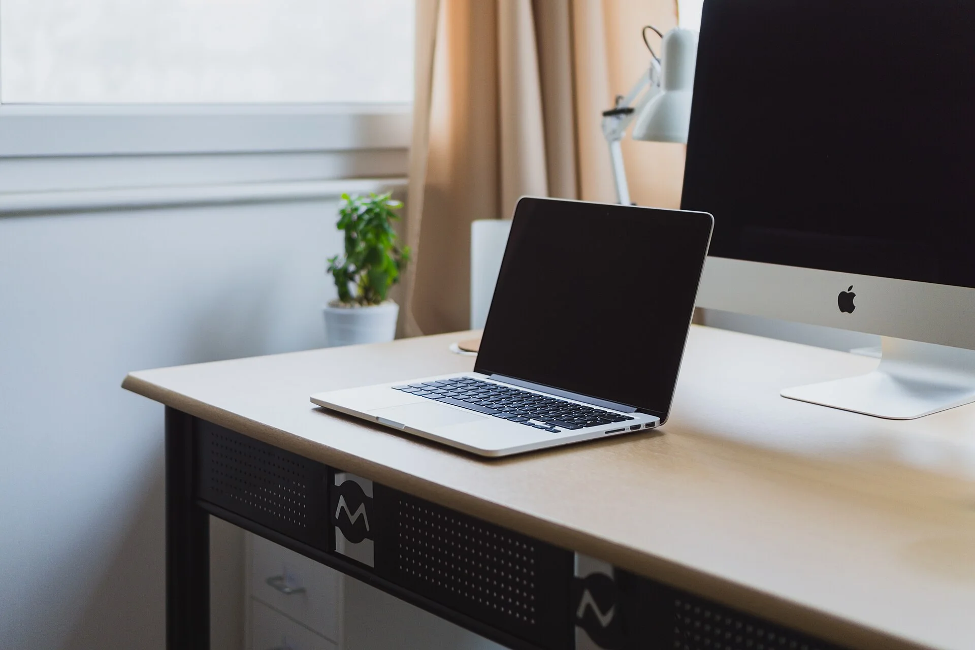 A laptop beside a window on an uncluttered wooden desk